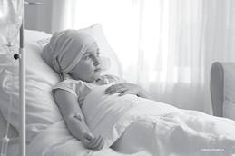 child laying in a hospital bed with an IV in her arm, wearing a scarf around her head.