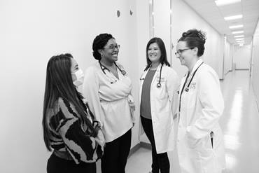 Four healthcare professionals in a hallway, smiling and talking together.