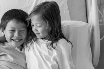 Young girl and brother in hospital bed laughing