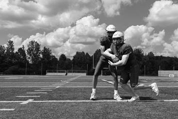 Two football players pass to each other, standing close on the field