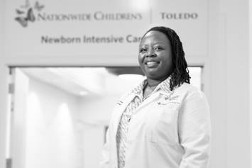 Dr. Smith is smiling in a hallway, wearing a white coat. The words "Newborn Intensive Care" are on the wall behind her.