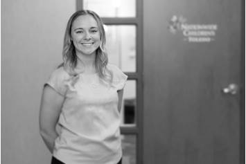 Megan is standing in front of a door with the Nationwide Children's Hospital Toledo logo on it. She smiling, with her arms behind her back.