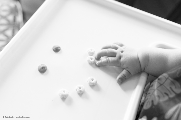 White plate with cereal on it and baby hands reaching for it