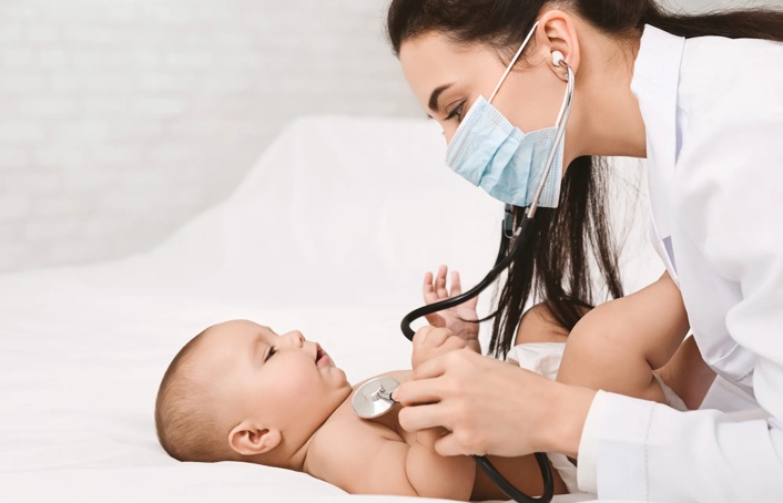 Doctor wearing a mask and listening to a baby's heart beat