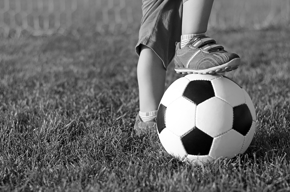 kids foot on top of a soccer ball in a grass field