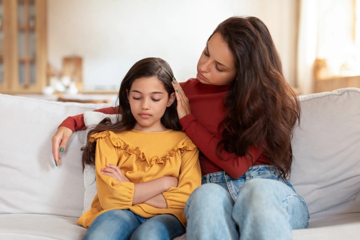 young girl sitting down with her mom's arm around her