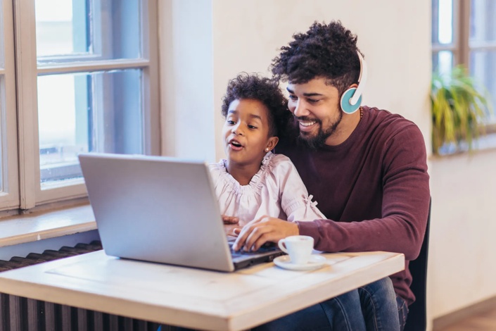 child sitting on his father's lap while they are using a laptop