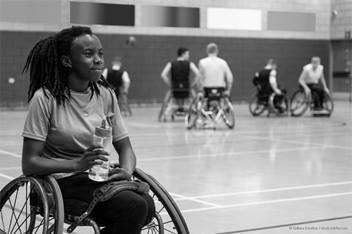 young woman in a wheelchair on a basketball court while holding a water bottle