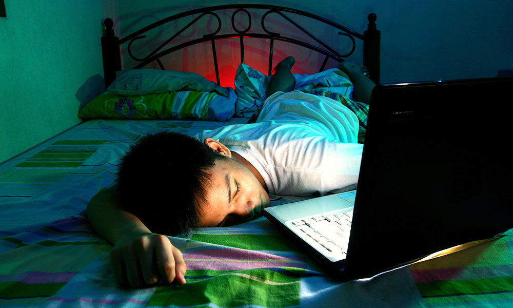 Boy sleeping on bed with computer on.