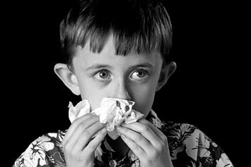 Child stopping a nosebleed with a tissue.