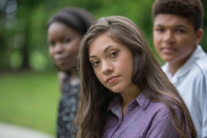 Young woman looking at camera with two friends sitting behind her.