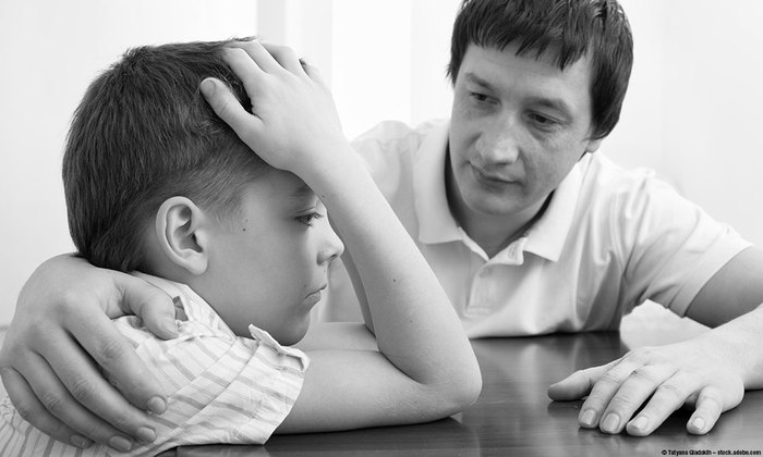 young boy with hand on his head looking sad with his father comforting him