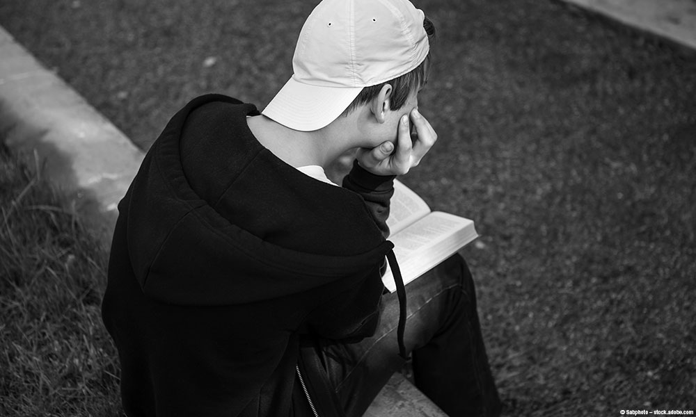 Teenager reading a book outside.