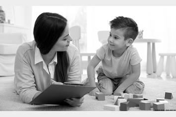 Women with clipboard and child playing with blocks laying on the board.