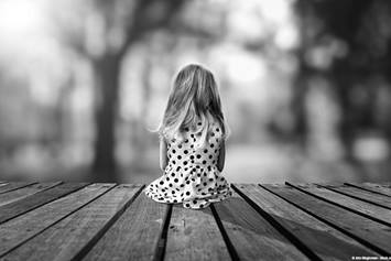 Little girl in polka dot dress sits alone in on a dock.