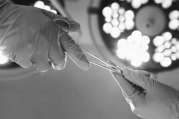 Surgeon with gloves holding a pair of scissors.