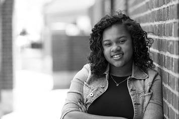 Adolescent girl leaning against a brick wall smiling