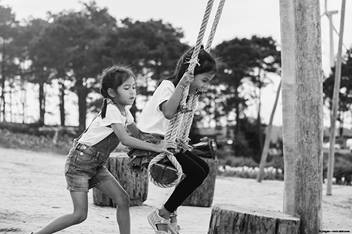 One kid pushing another kid on a swing set