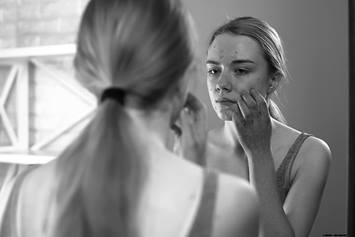 Teenager girl looking in the mirror touching her face