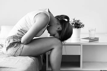 Teenage girl holding her stomach, bent over on her bed