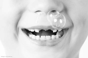 child missing their two front teeth blowing a bubble out of their nose