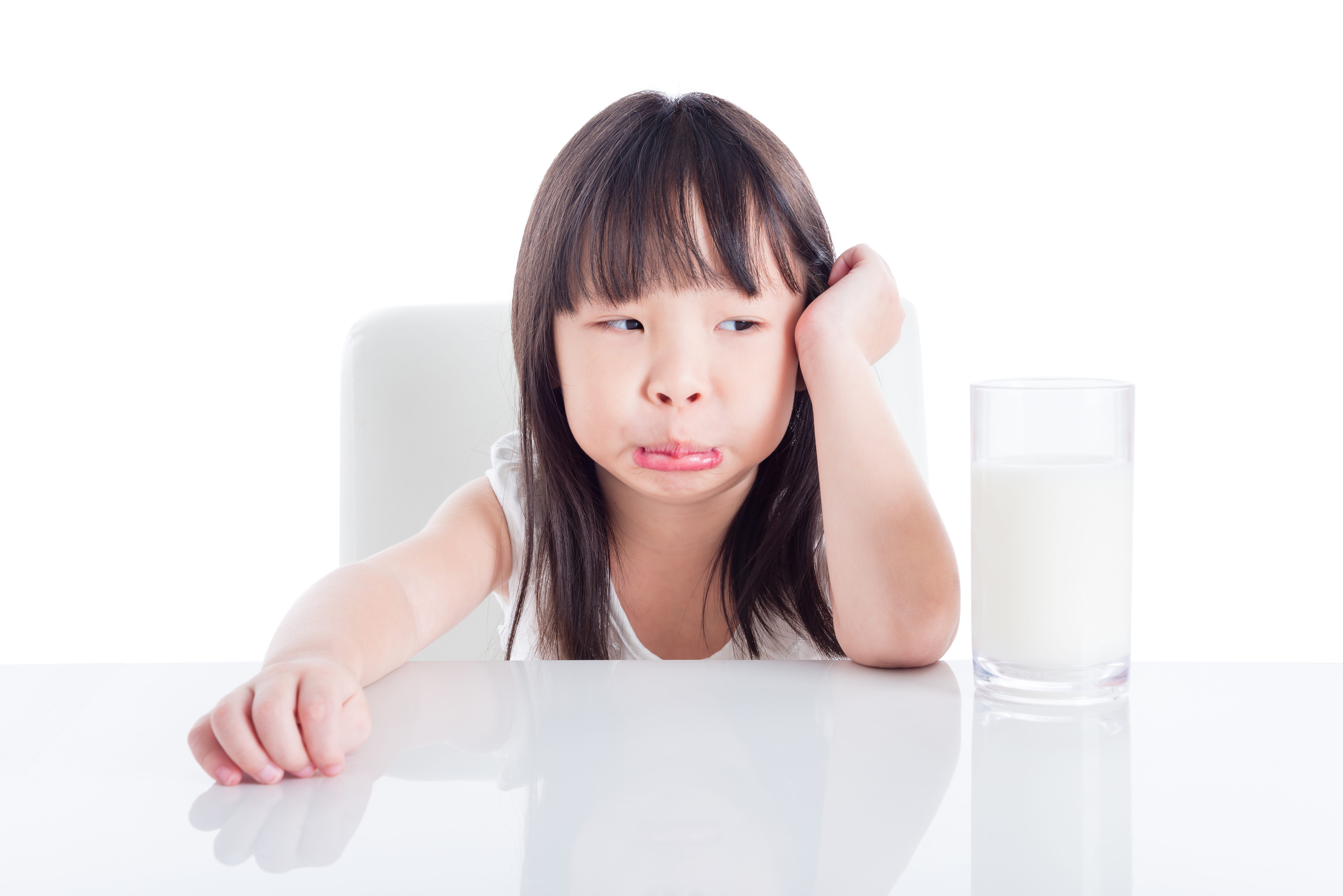 young child sitting with her elbows on a table with a glass of milk