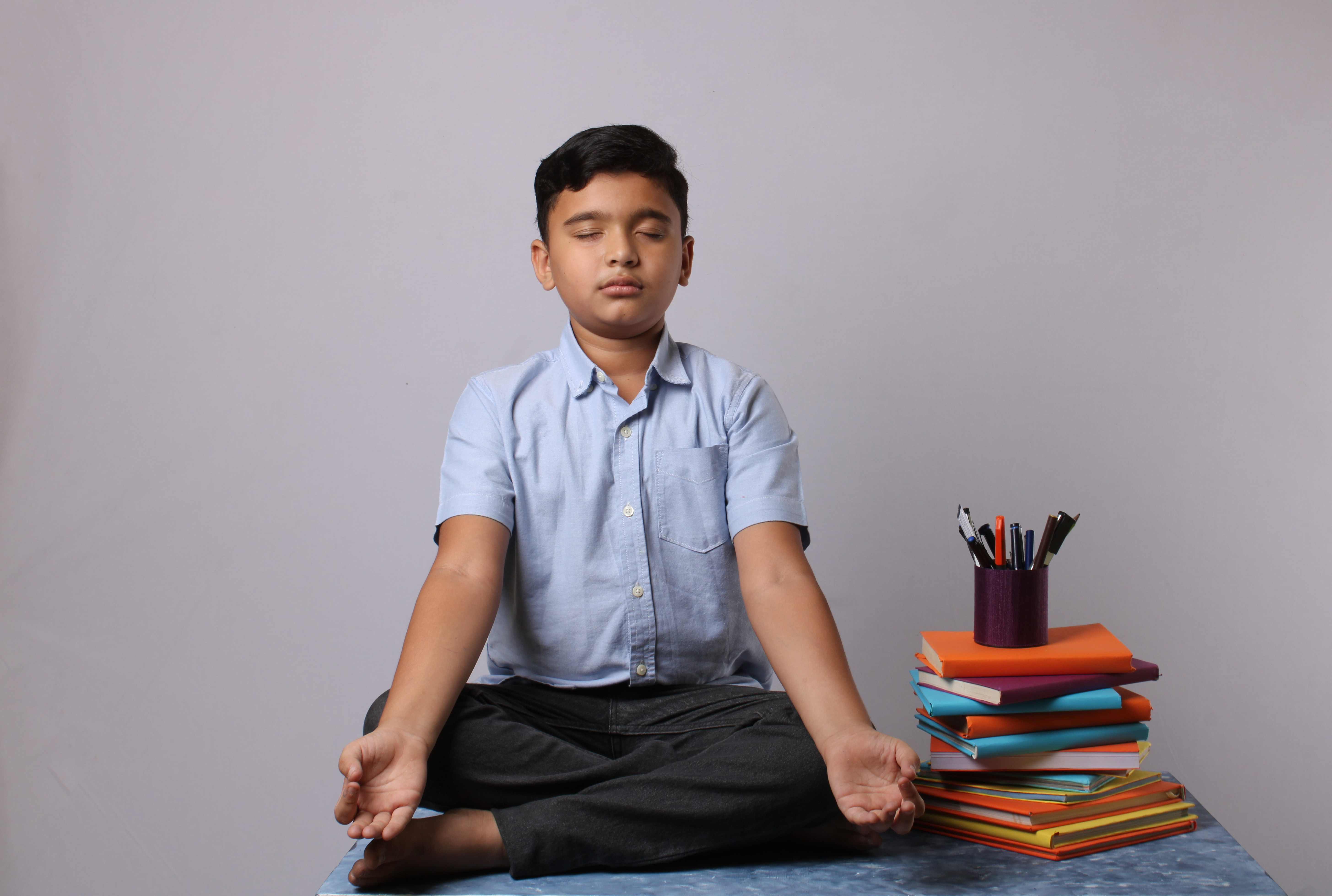 child meditating next to a pile of books