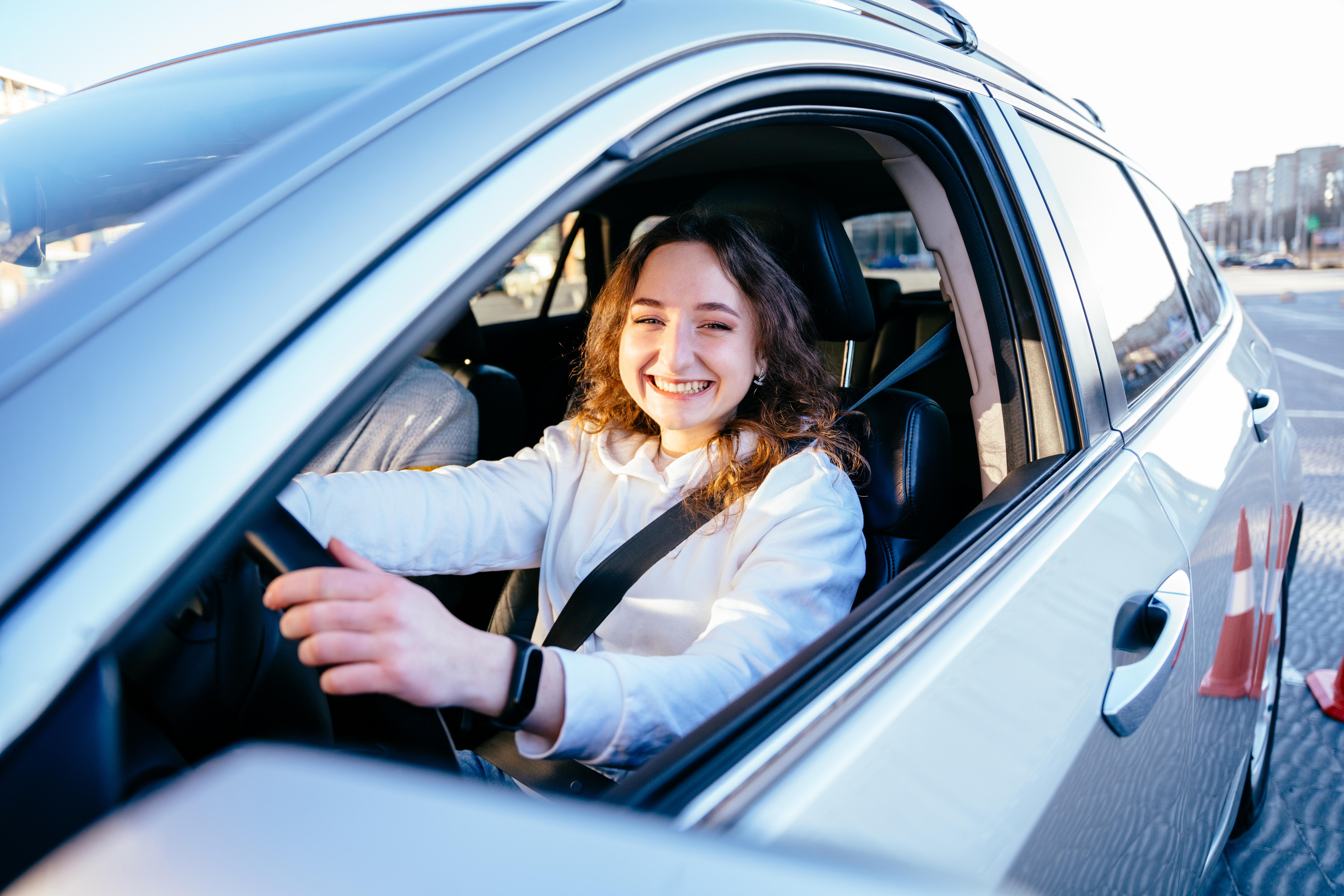 young woman is smiling behind a car steering wheel