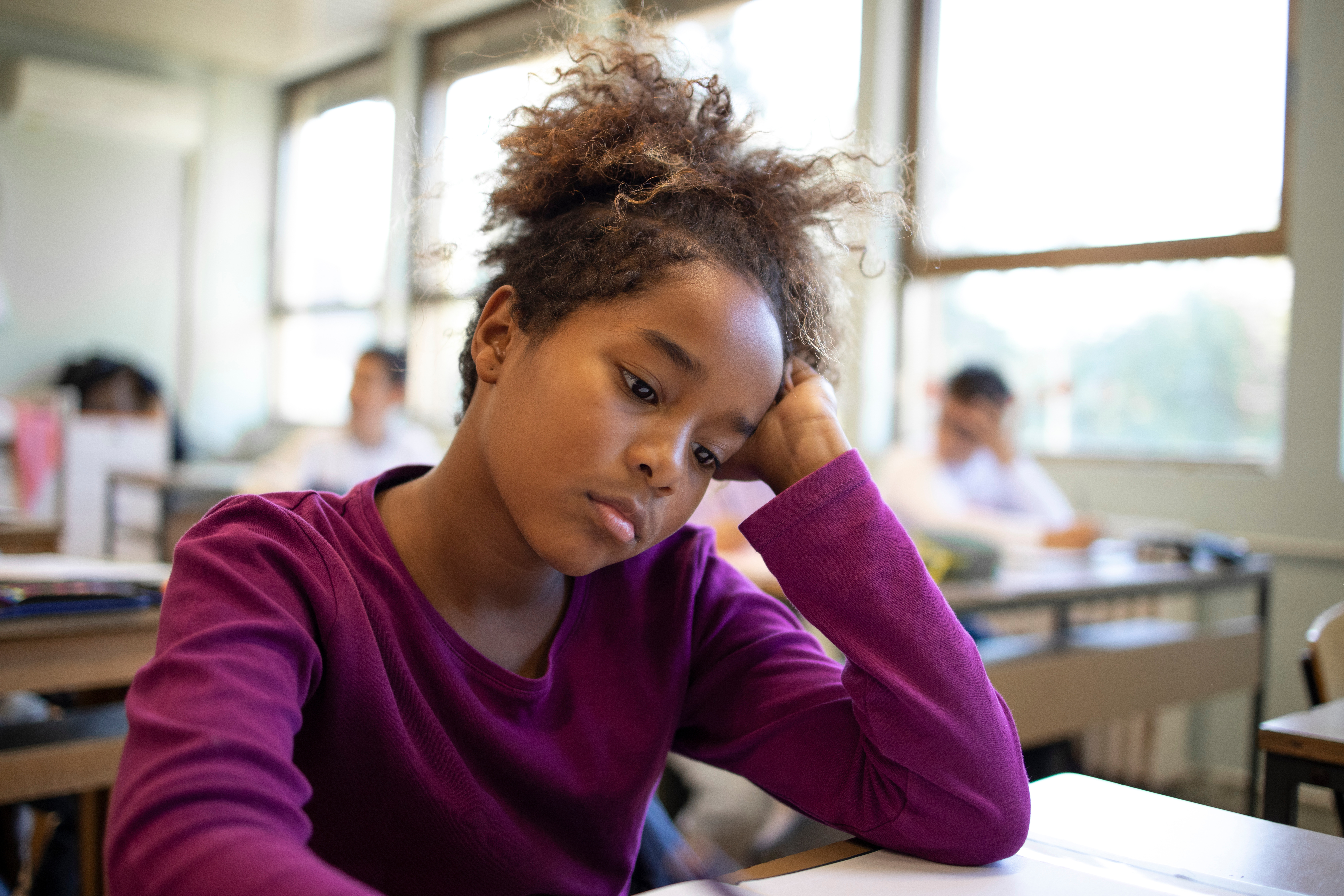 young child sitting at their desk at school looking sad