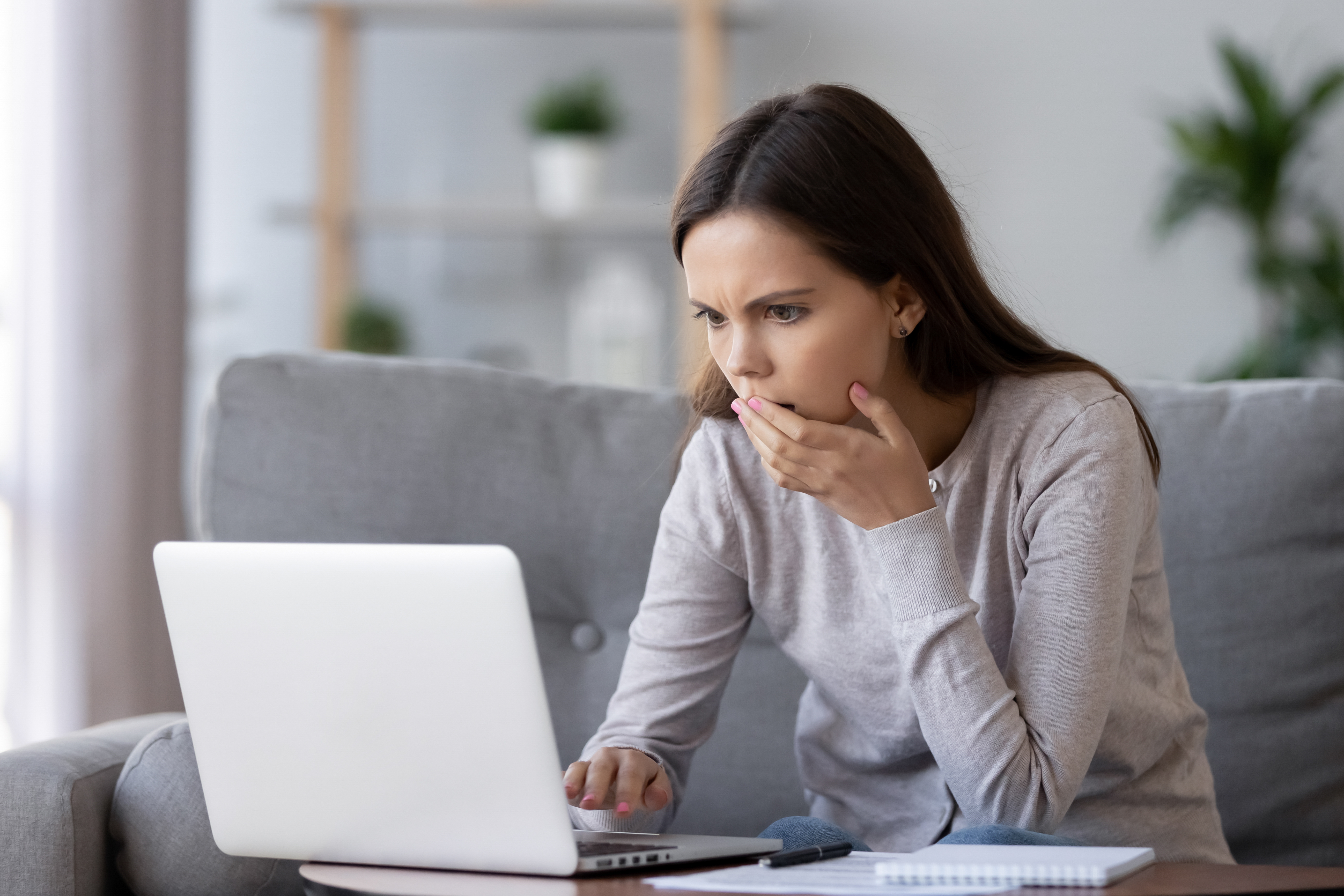 young lady sitting at a laptop with her hand over her mouth, looking concerned
