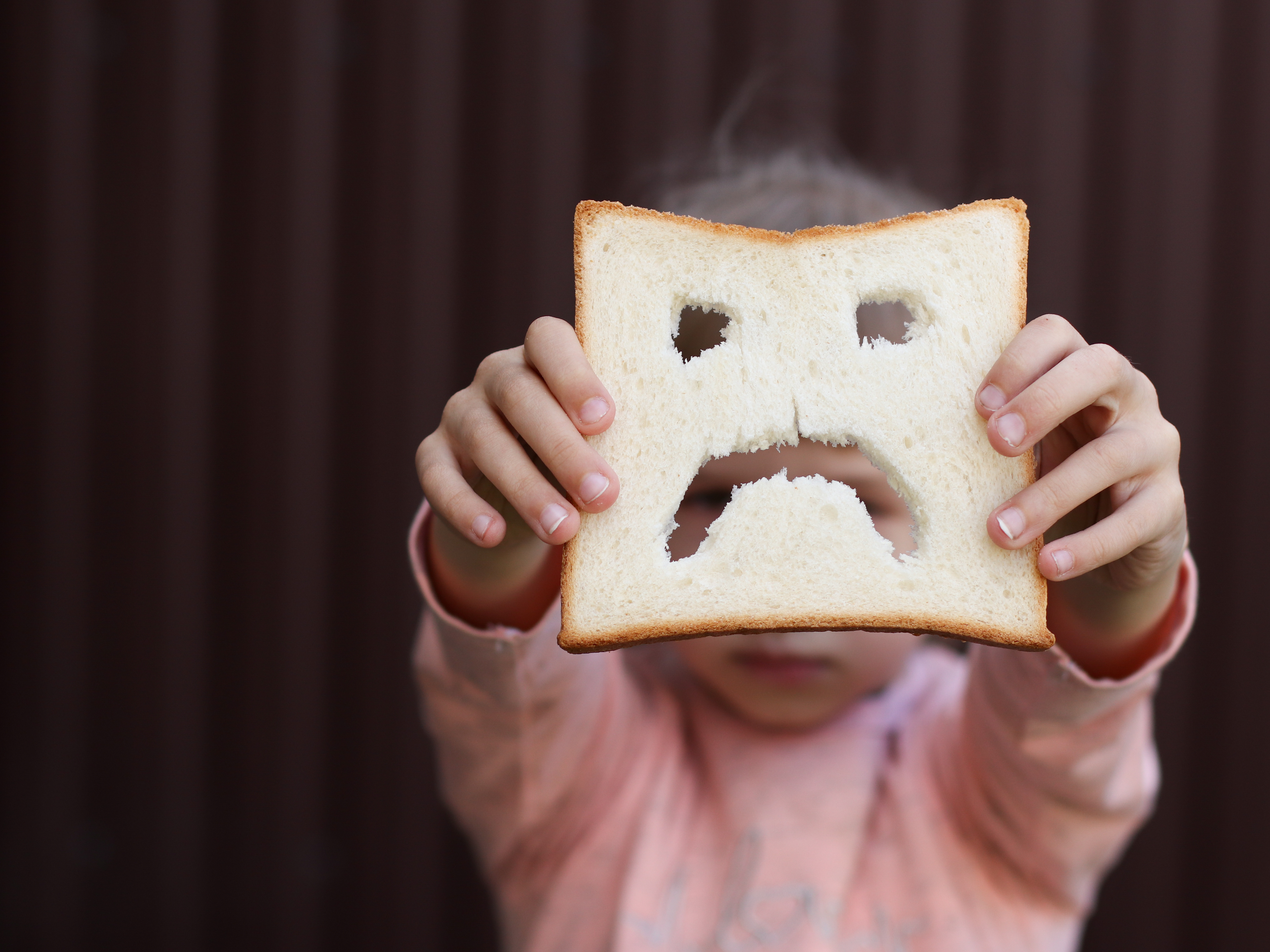 Child holding out a sandwich with a sad face cut out of it