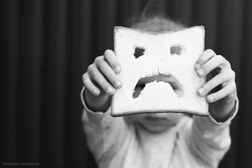 Child holding out a sandwich with a sad face cut out of it