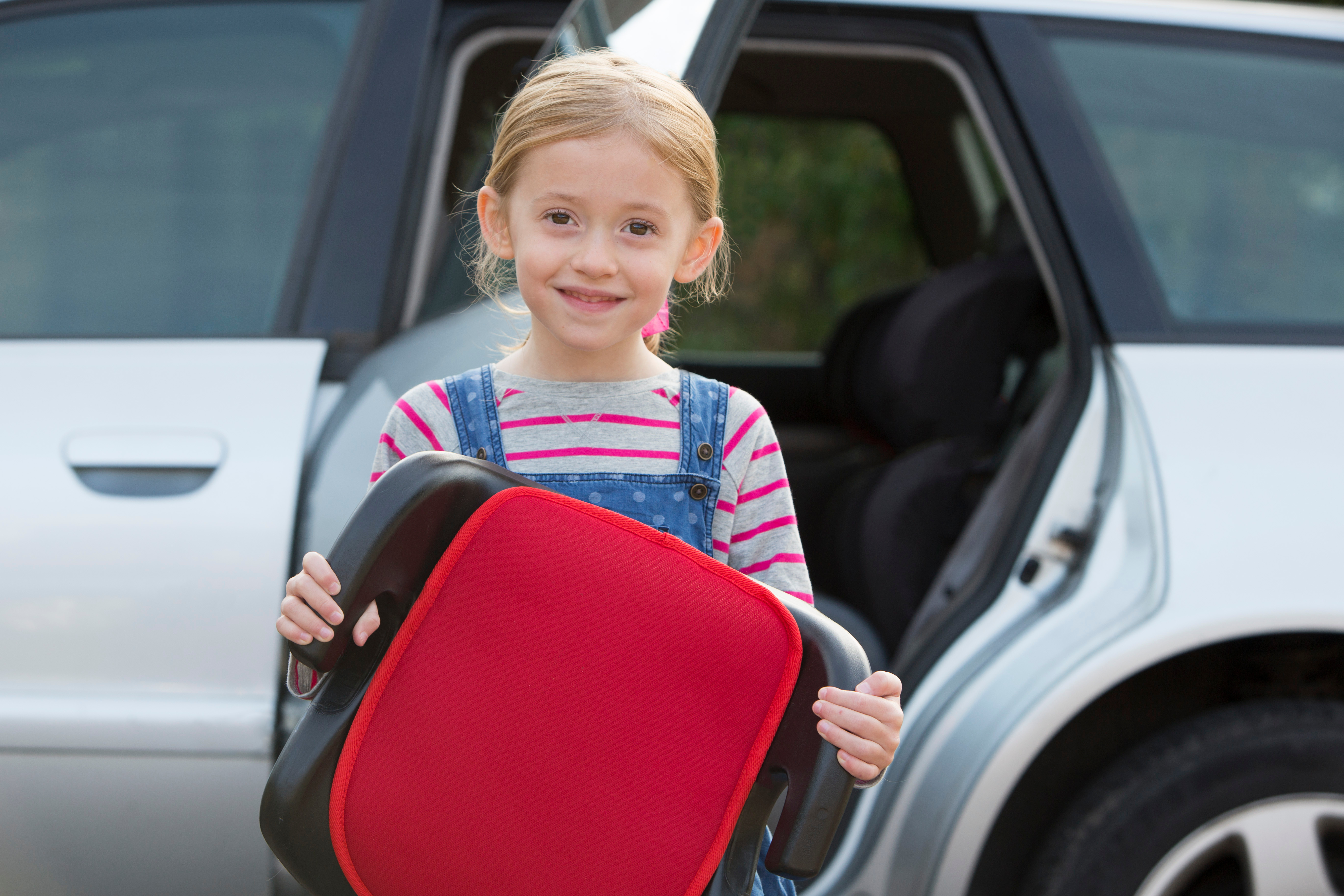 young girl holding a car seat outside of a car