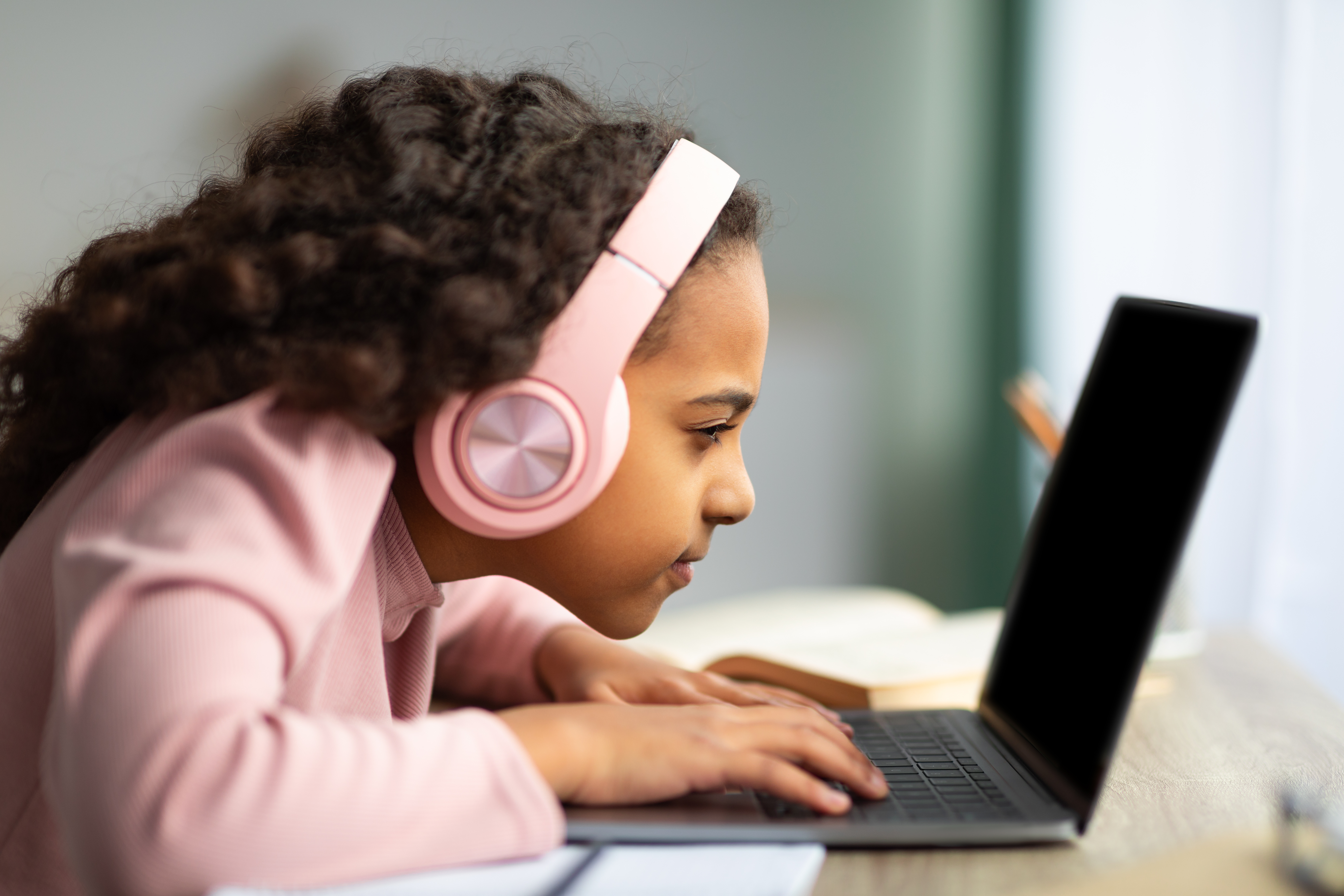 young child looking closely at a computer screen with white headphones on her head
