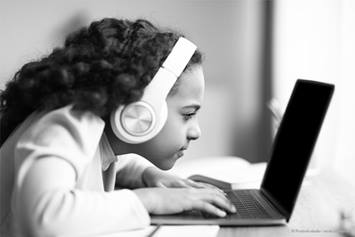 young child looking closely at a computer screen with white headphones on her head