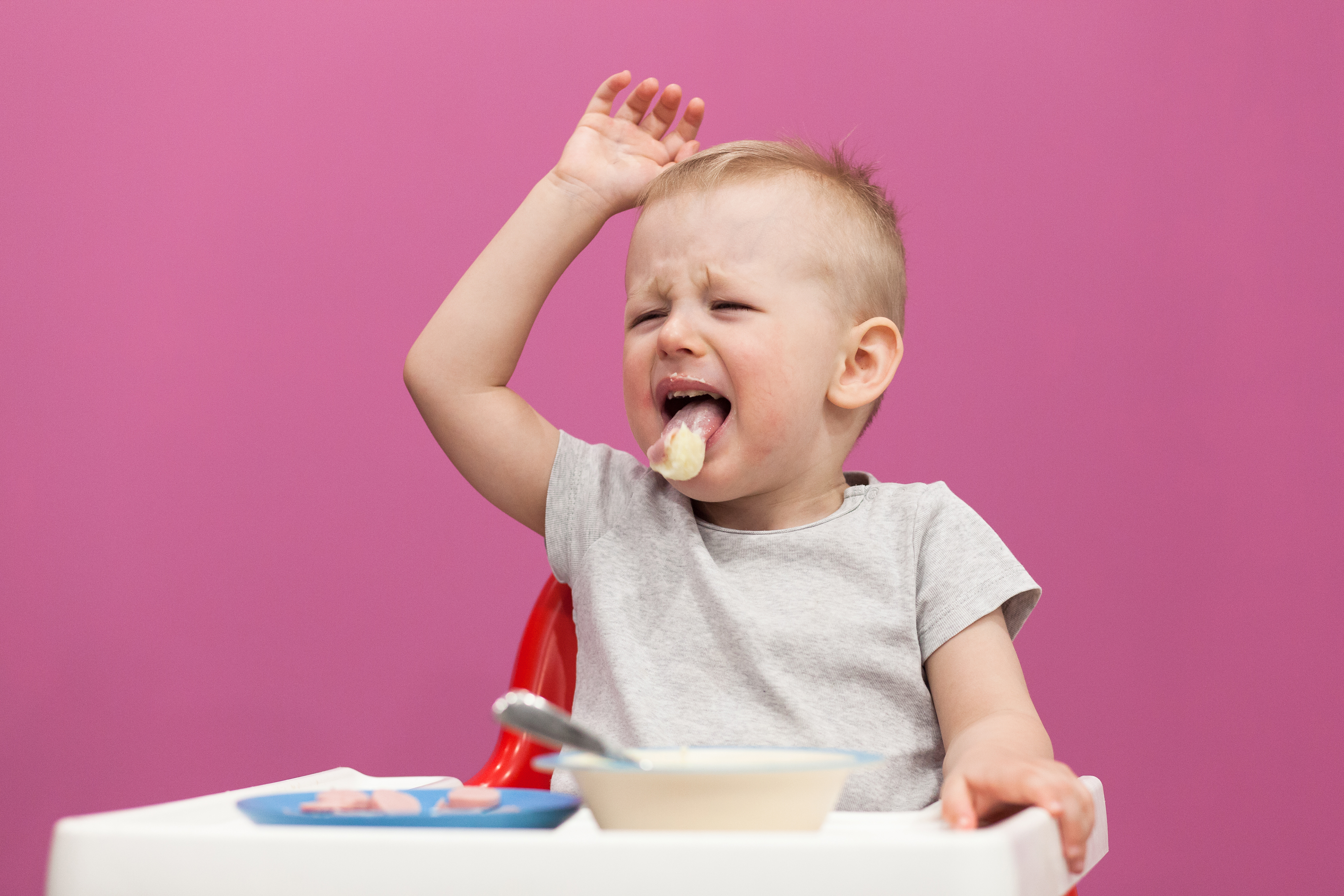 child sitting in his kitchen chair and doesn't seem to like his food