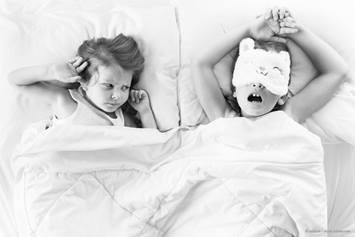 2 girls laying in bed, one plugging her ears and one is snoring