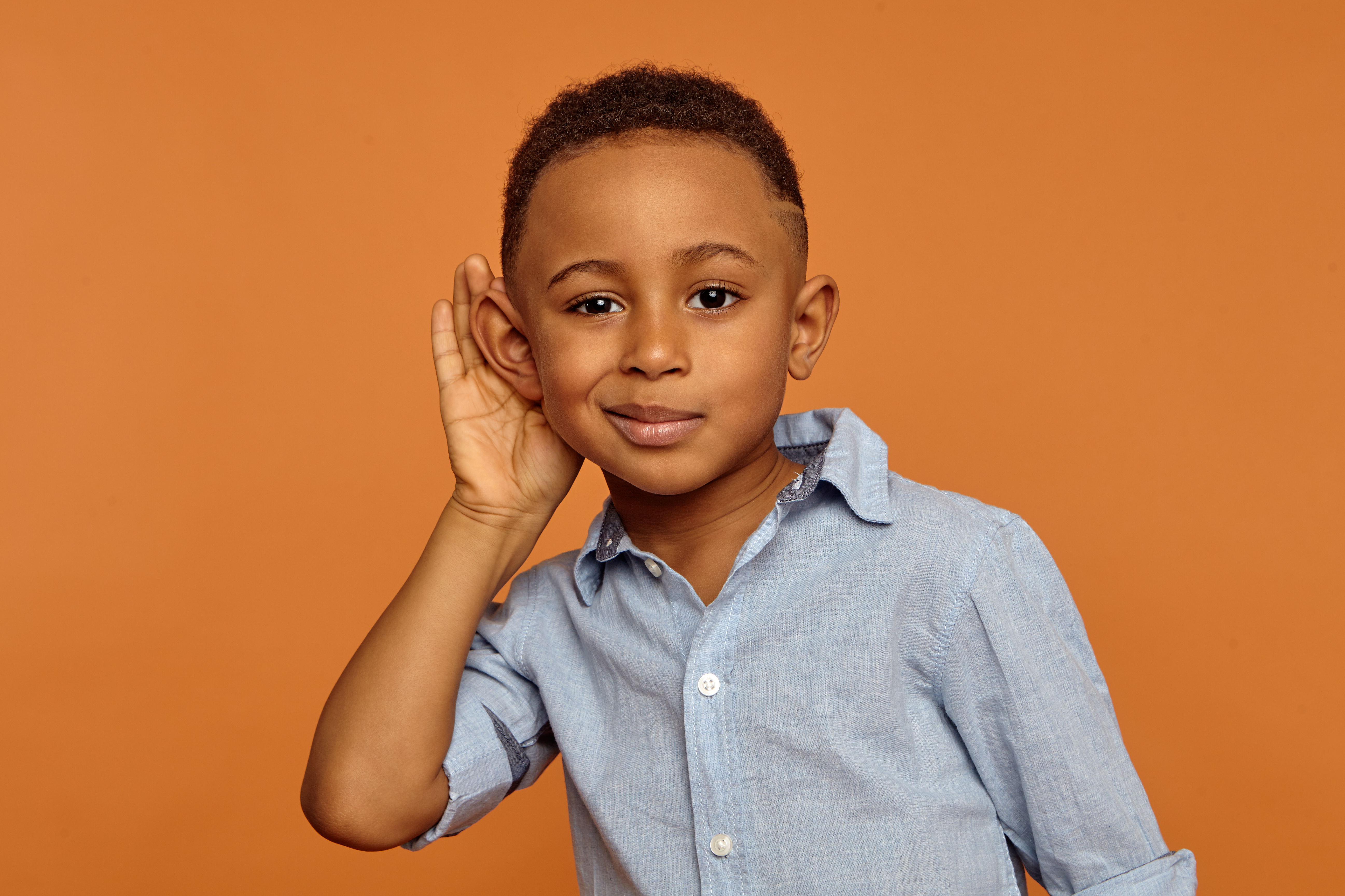 young boy with his hand up to his ear like he is focusing on listening