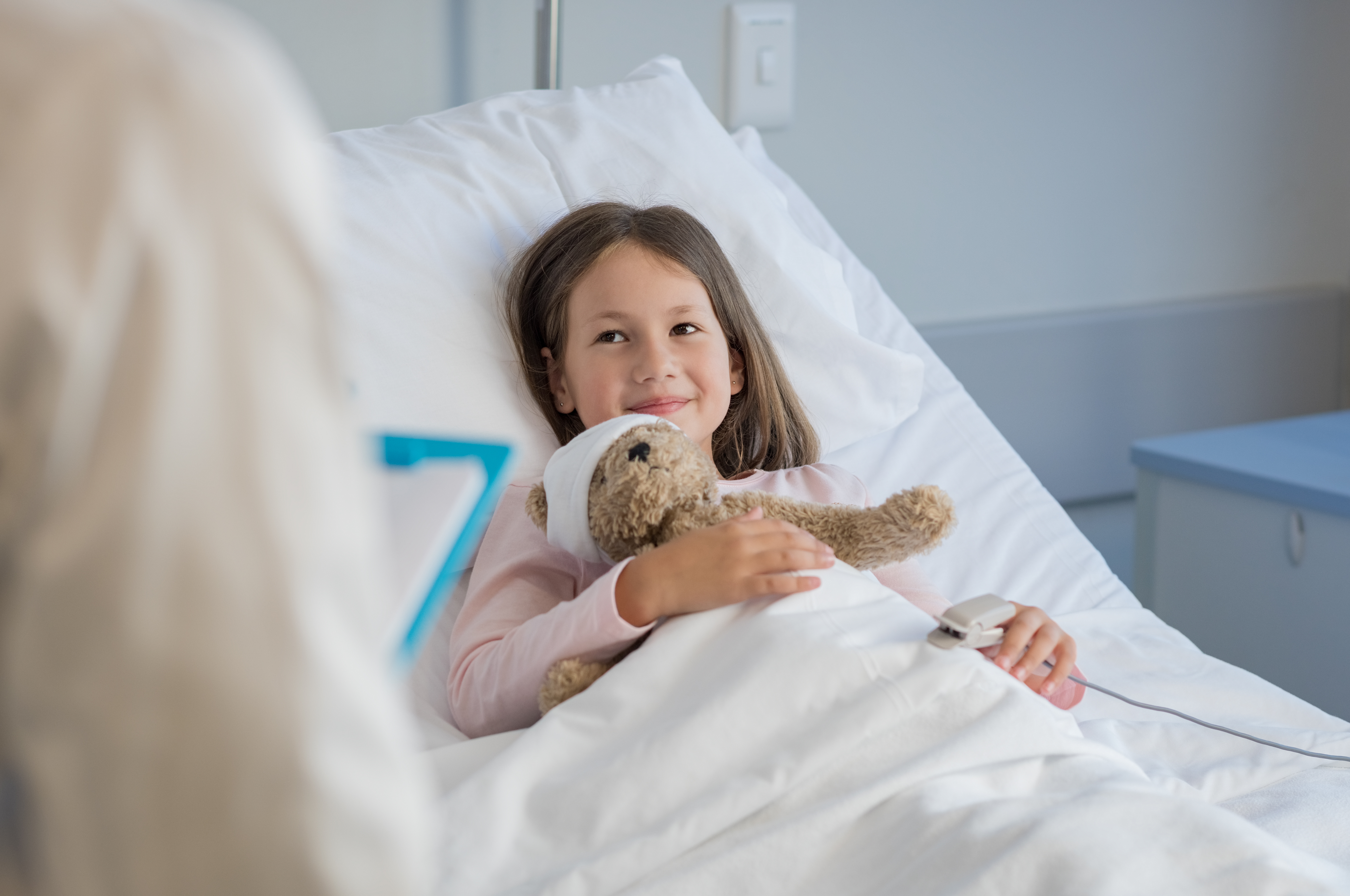 young girl in a hospital bed, holding her teddy bear