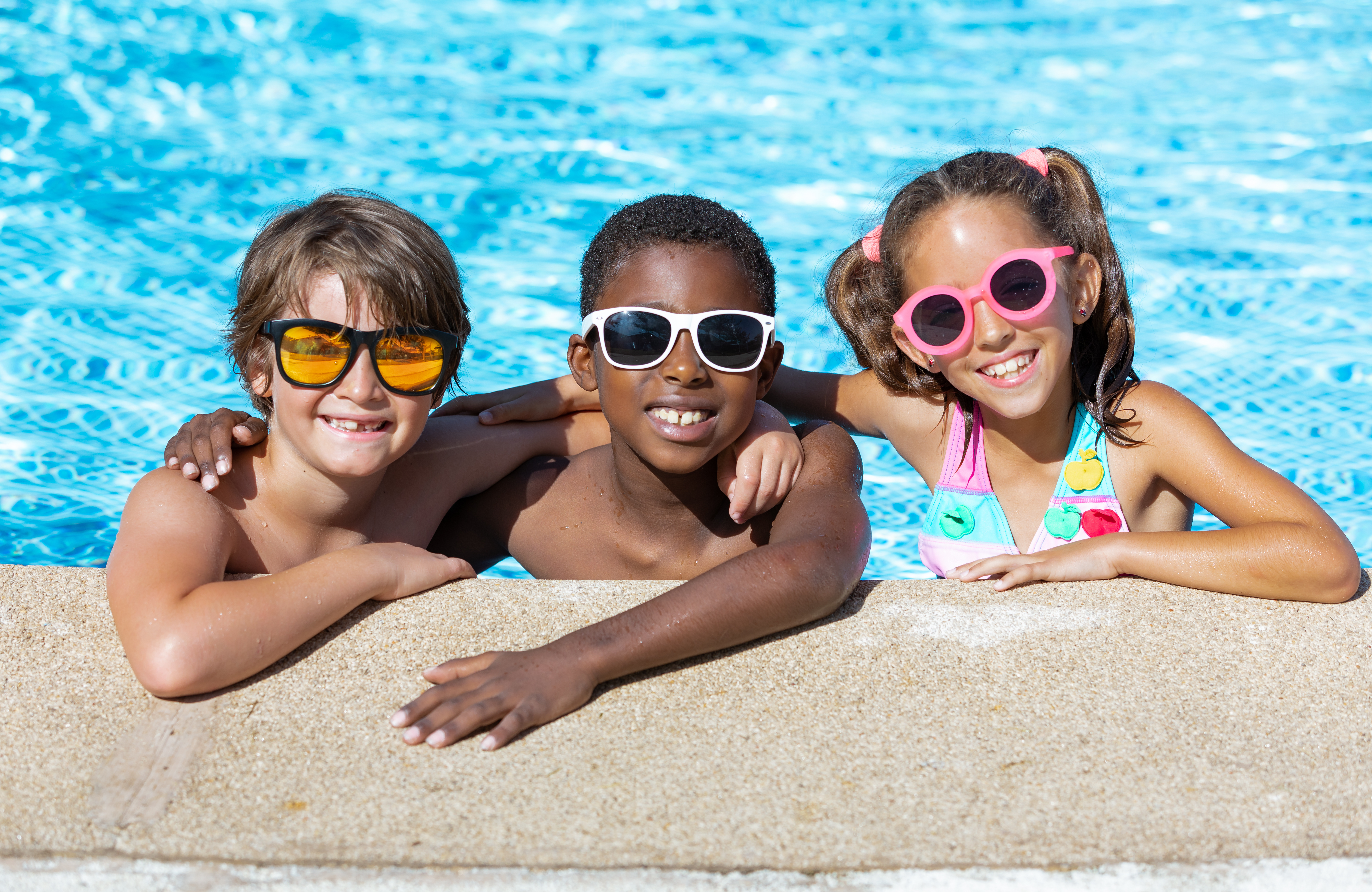 three kids smiling in a pool with their sunglasses on