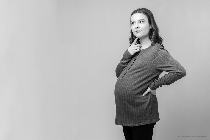 Pregnant mother standing with her finger on her chin.