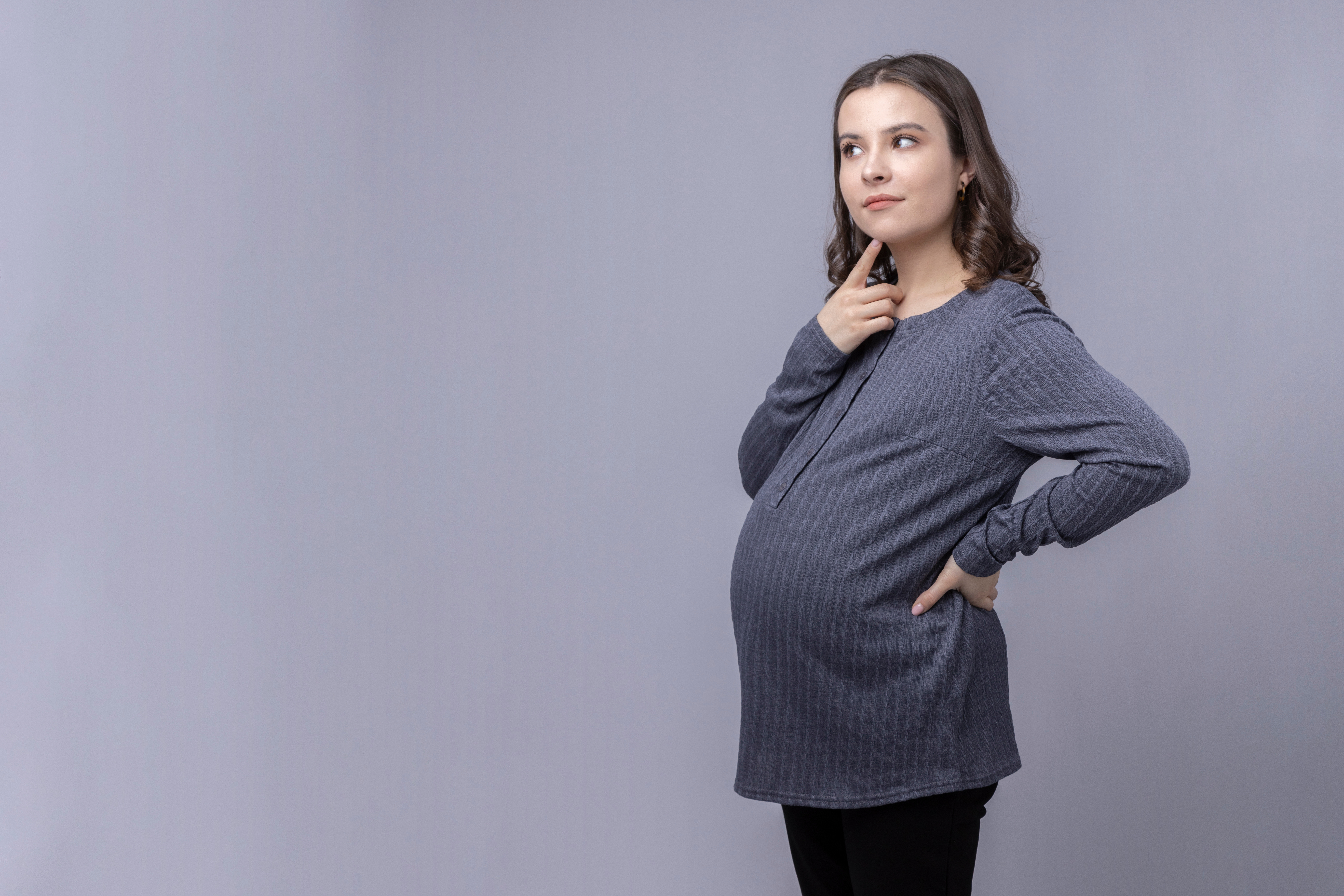Pregnant mother standing with her finger on her chin.