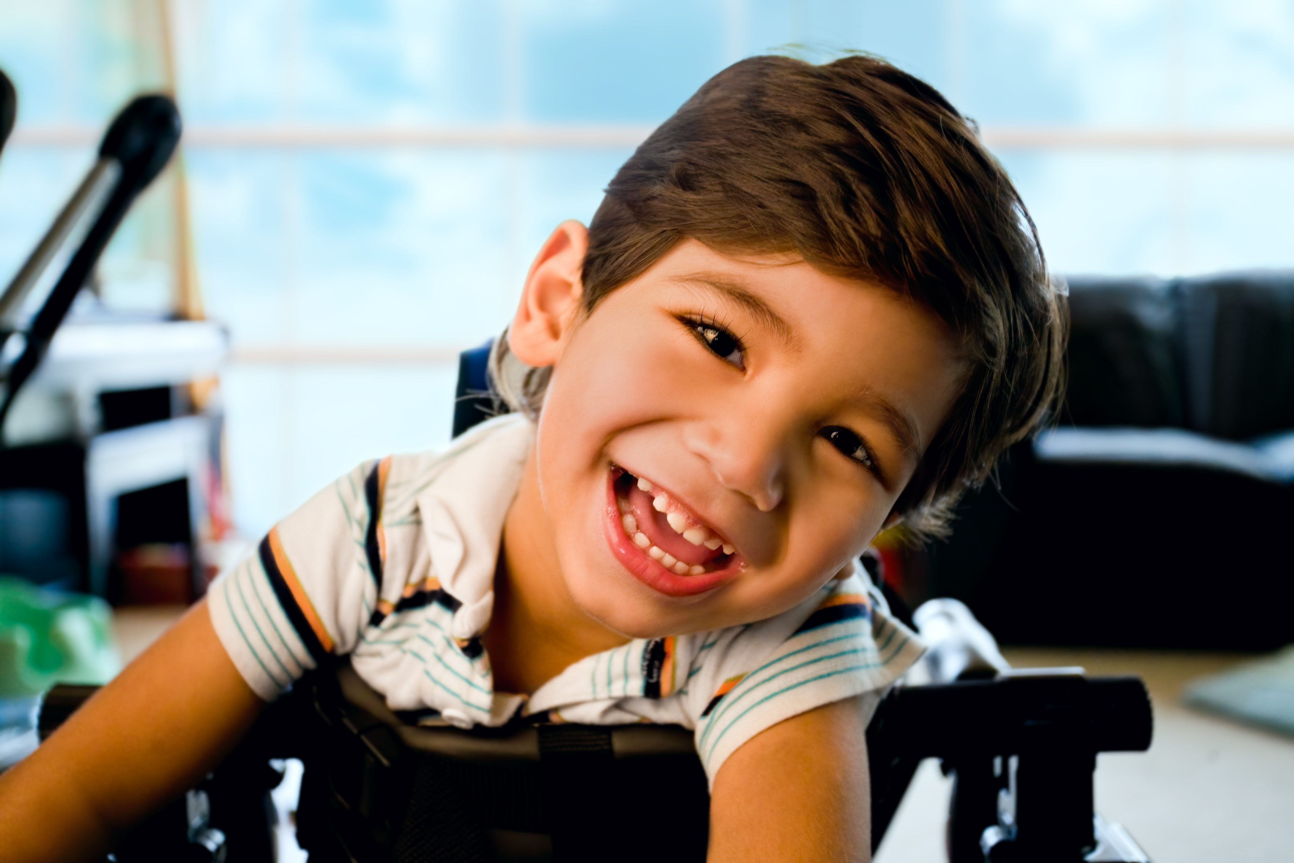 young boy, wearing a striped shirt, smiling at the camera over the back of a chair