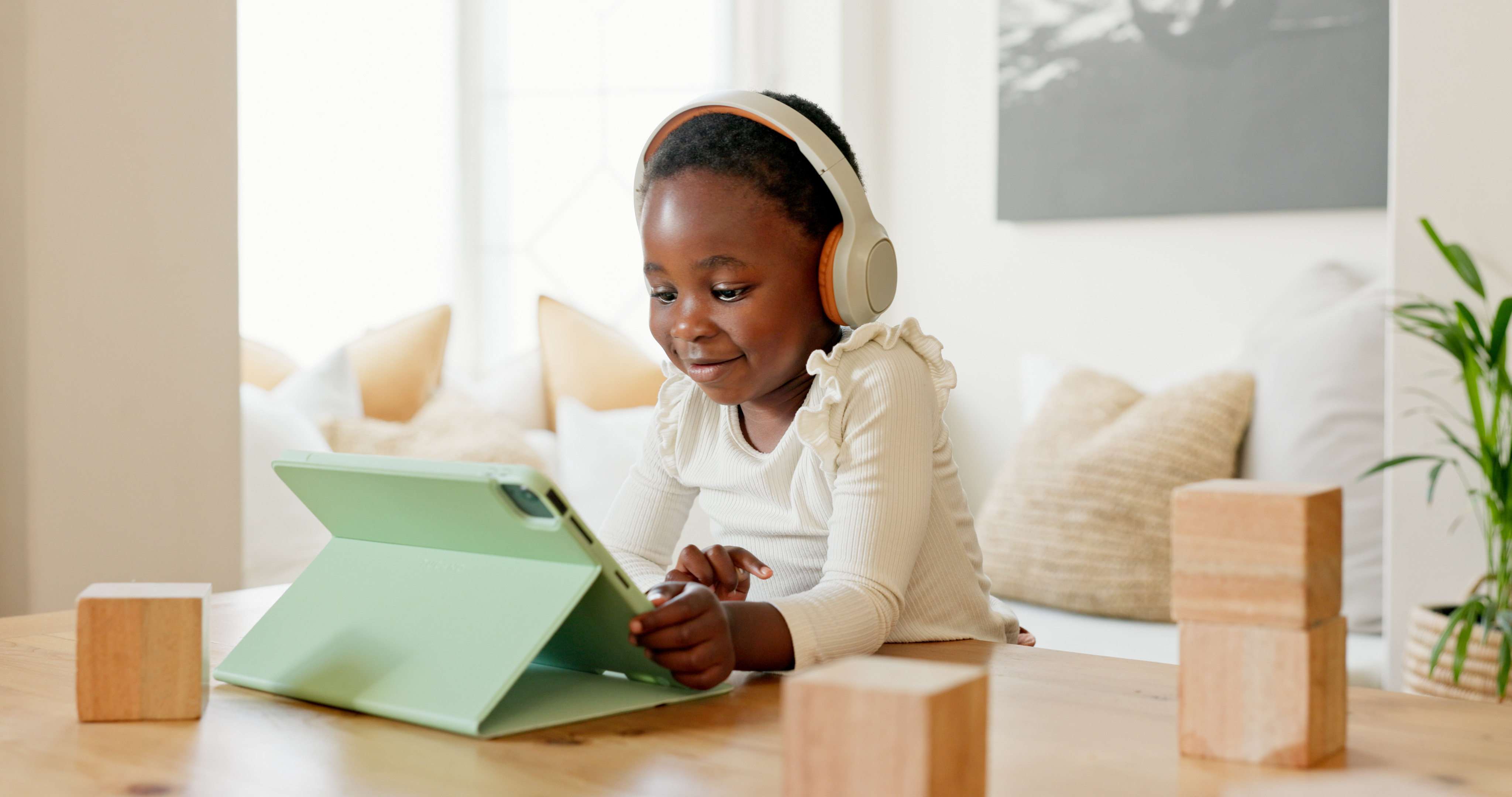 child sitting at a table with her headphones on while looking at an ipad