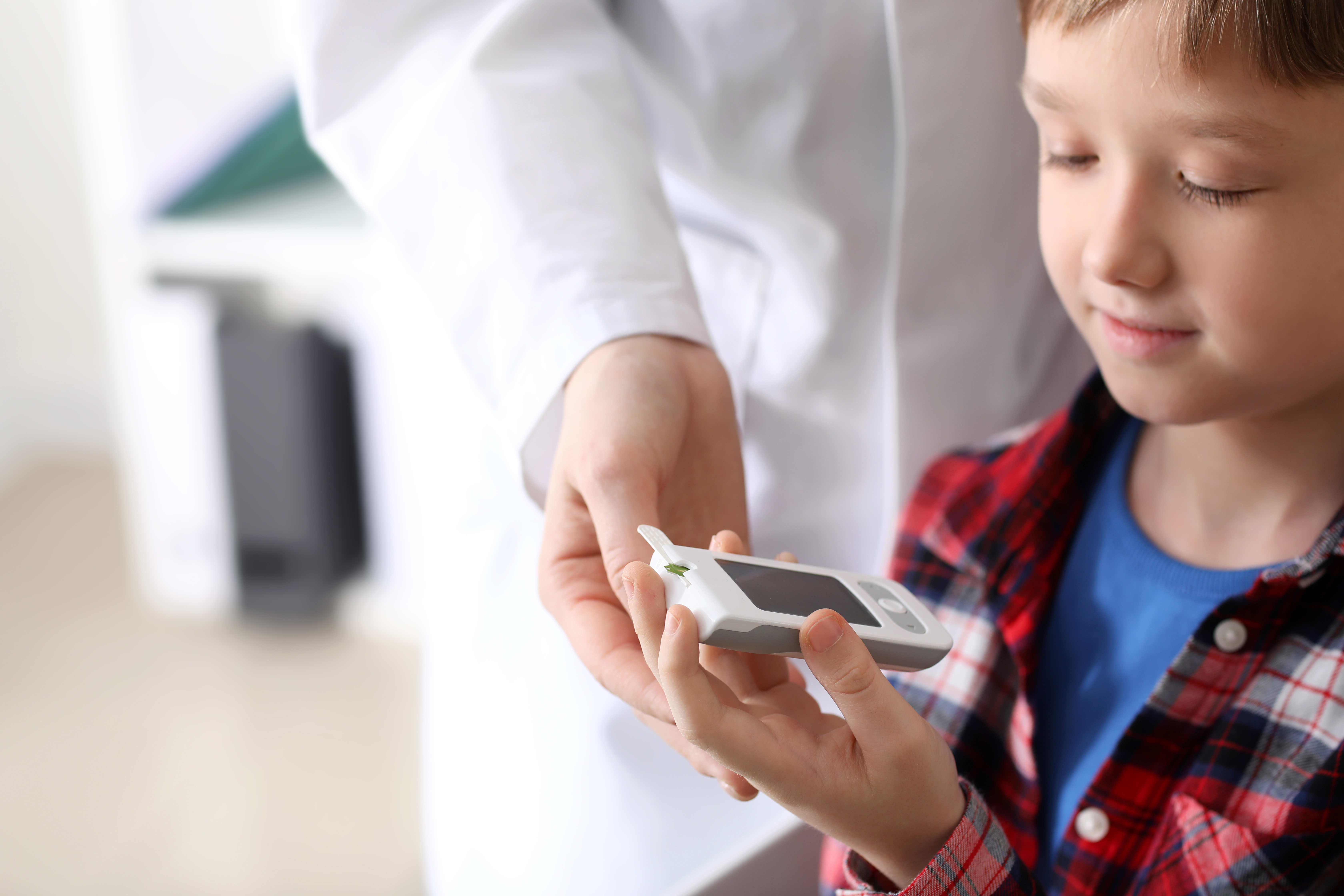 young boy checking his blood sugar with the doctor's assistance