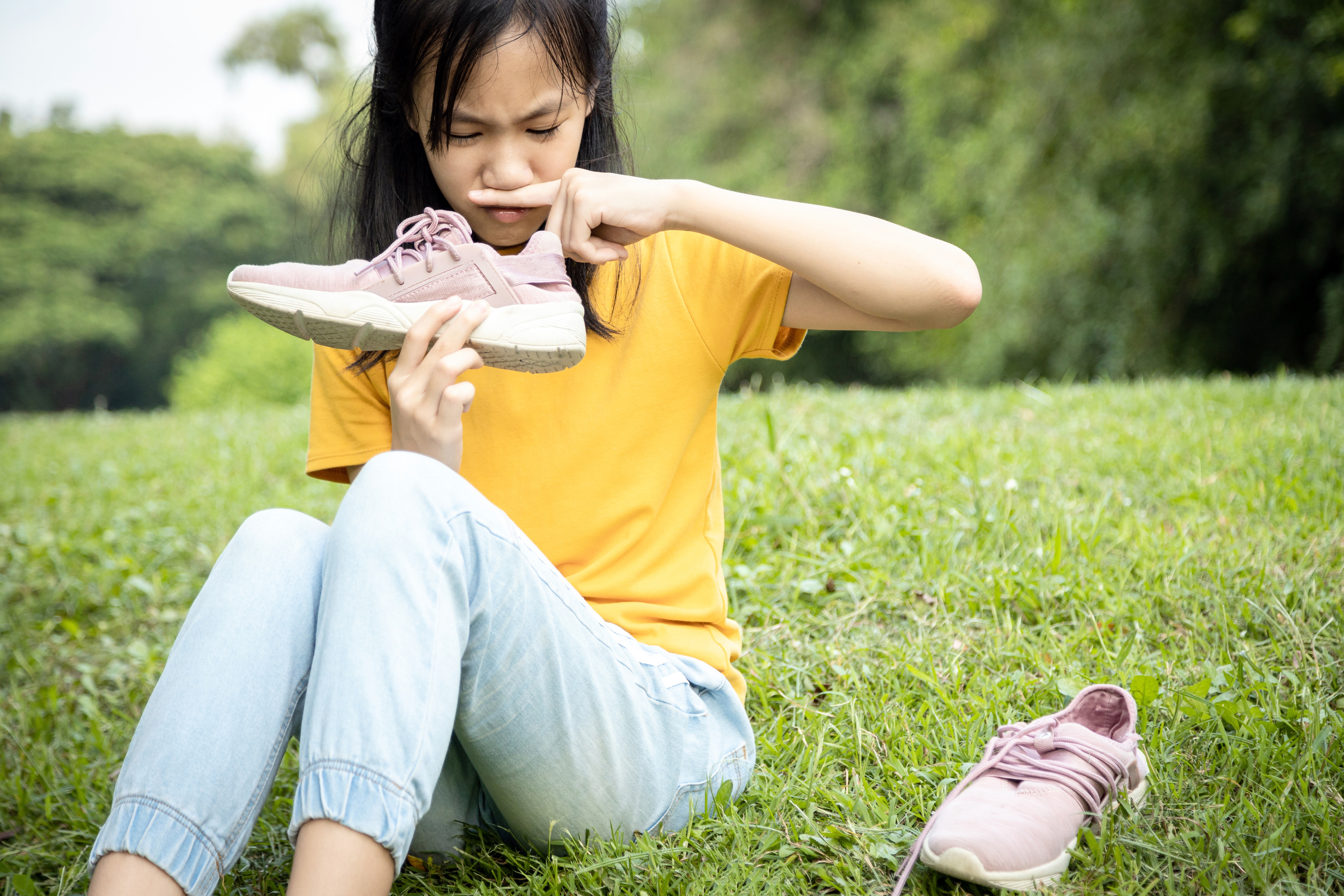young girl holding her shoe up to her nose in disgust