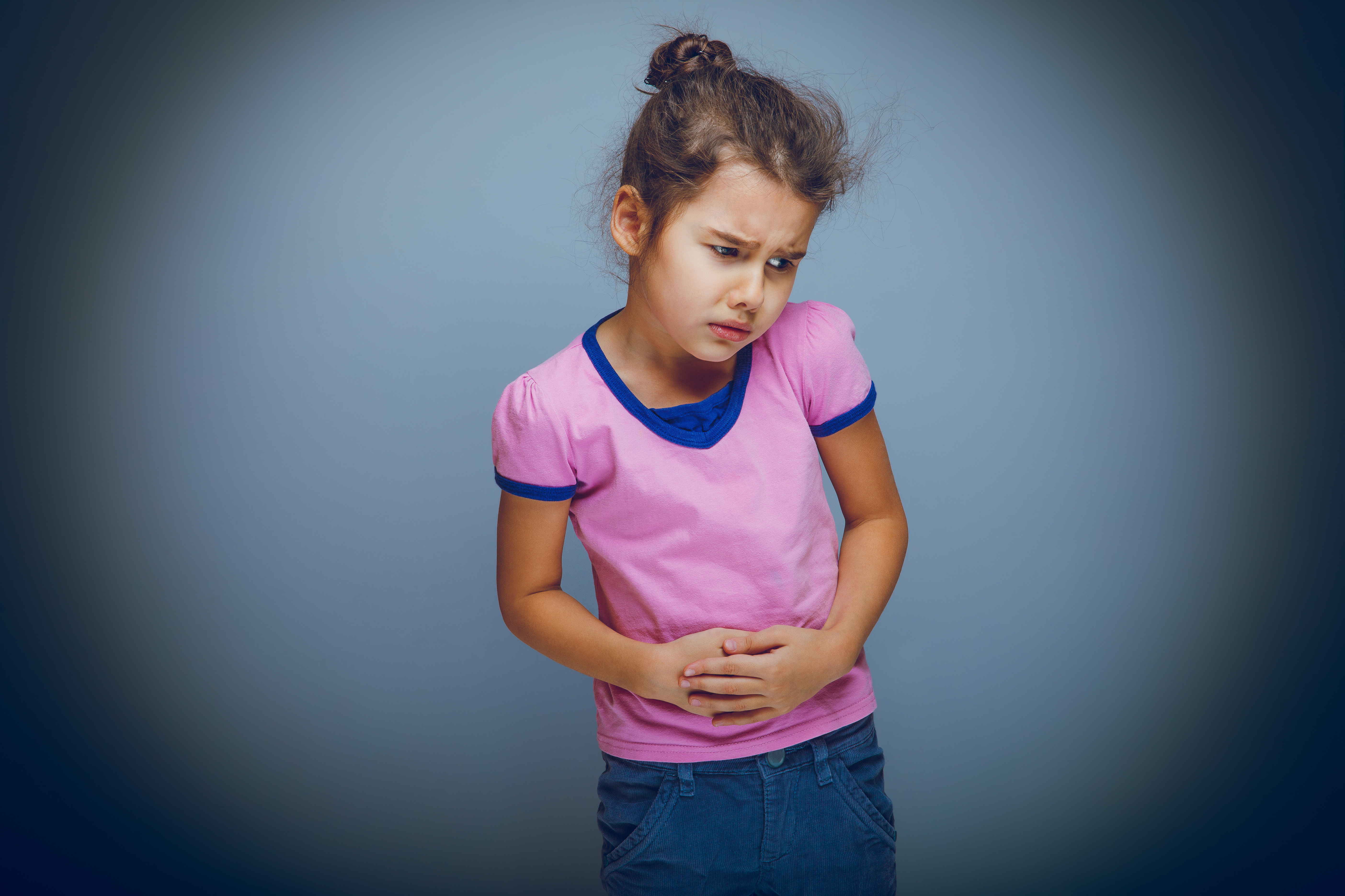 A young girl in a while shirt is gripping her stomach while grimacing in pain.