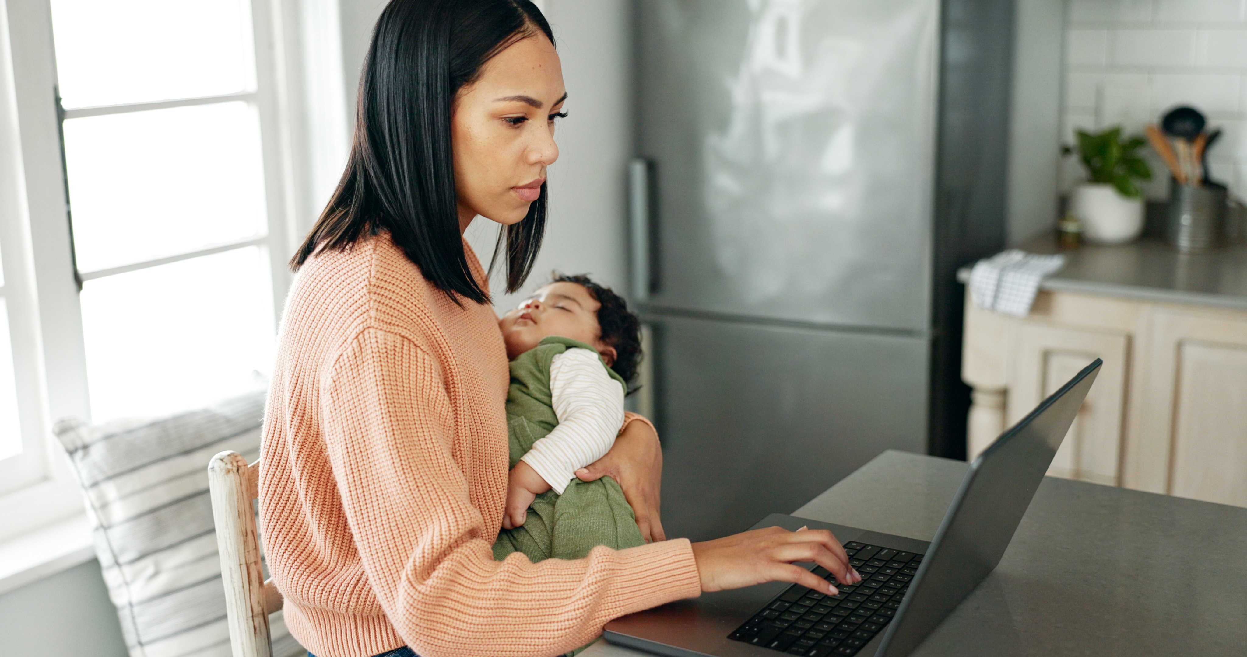 mother holding her baby in one hand while working on the computer