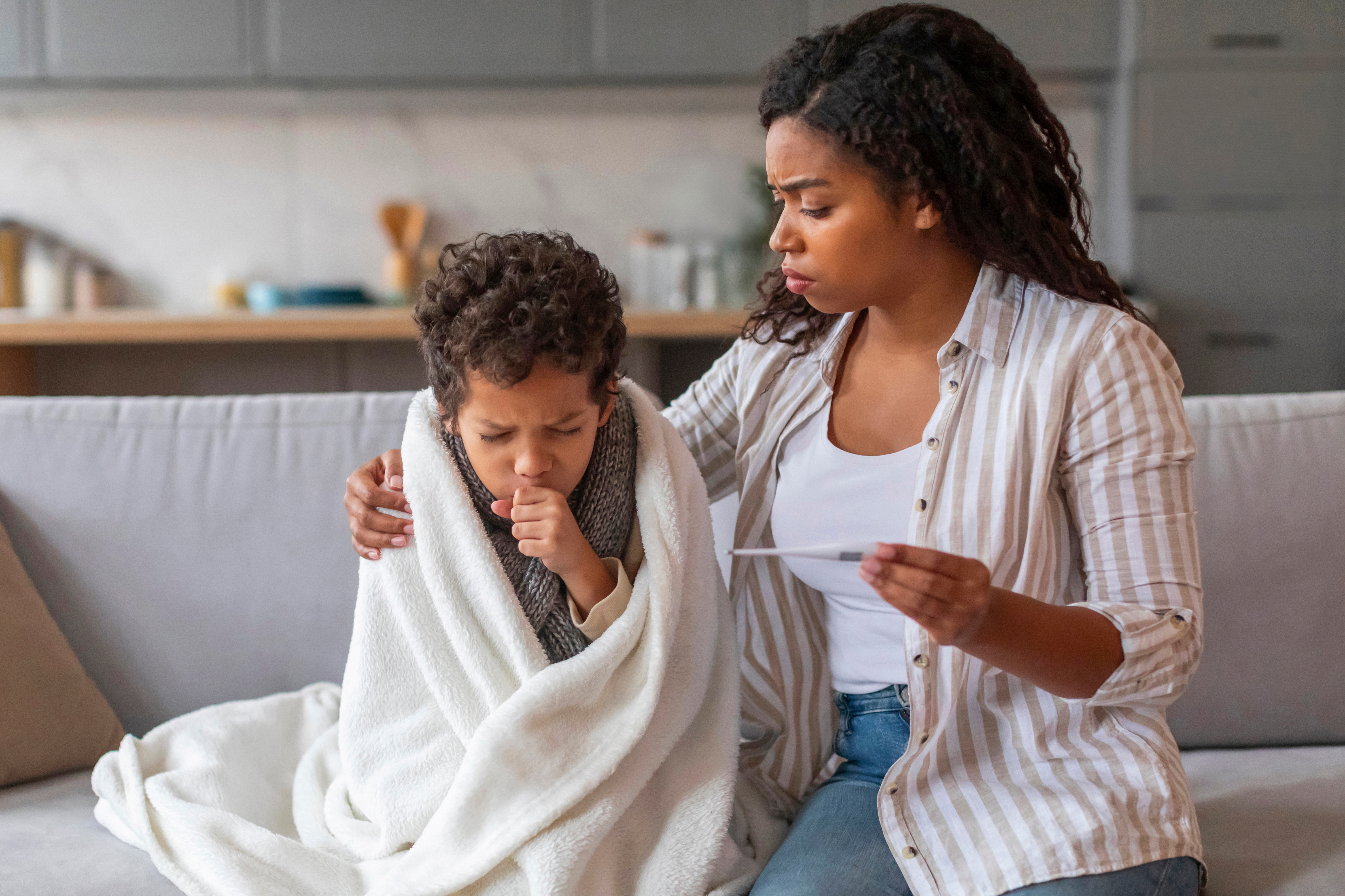 Mother taking the temperature of a young sick boy wrapped in a blanket