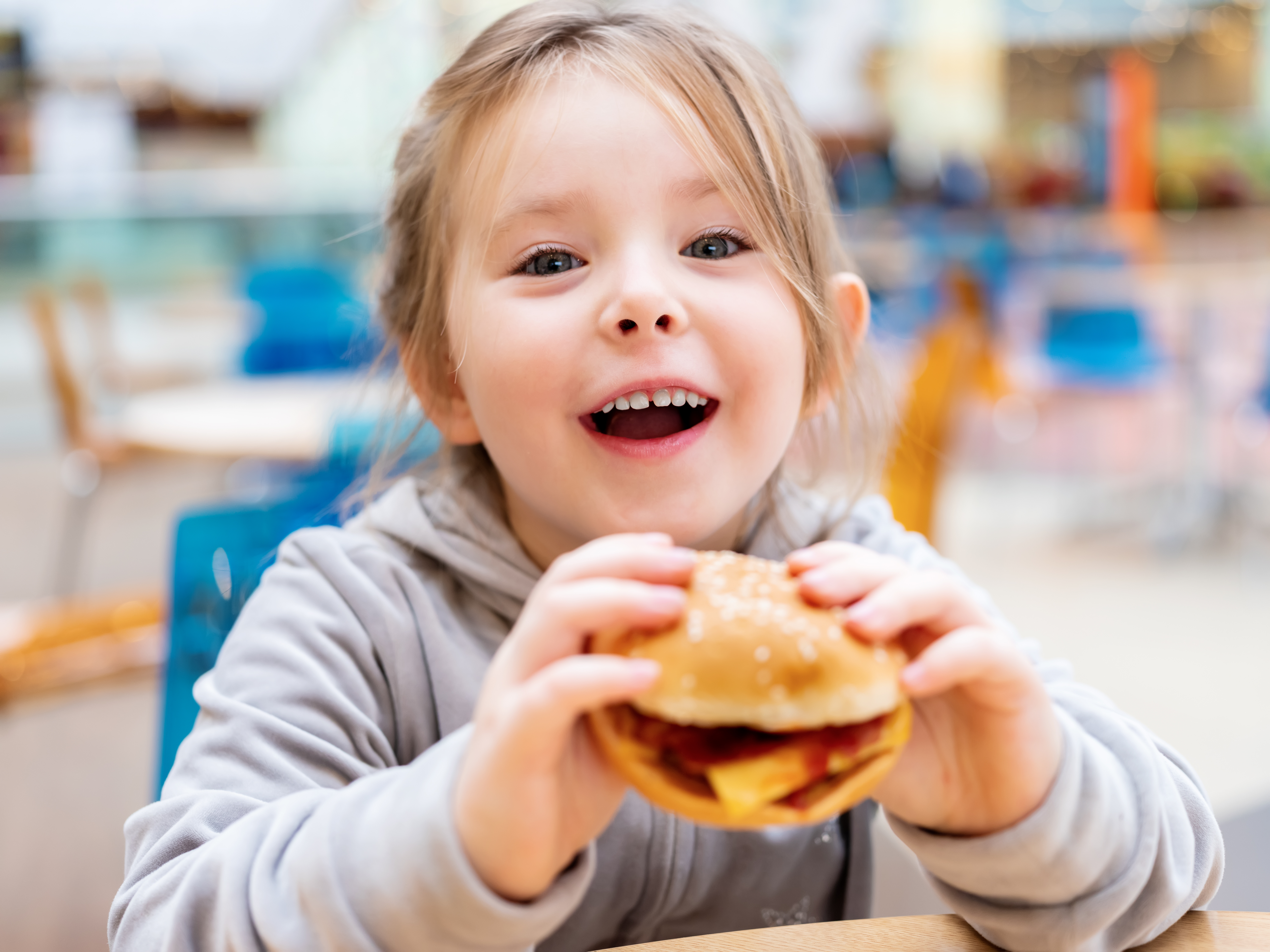 young girl around the age of 5 with a burger in her hands as she smiles at the camera
